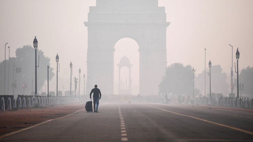 A man with a suitcase walks towards Delhi's India Gate shrouded in smog