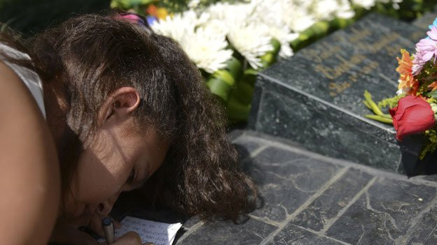 Girl writing note at grave of Pablo Escobar