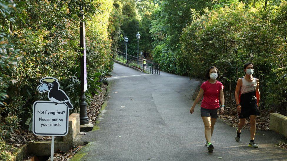 People wearing face masks against Covid walk past a sign encouraging the use of masks at Singapore's Botanic Gardens