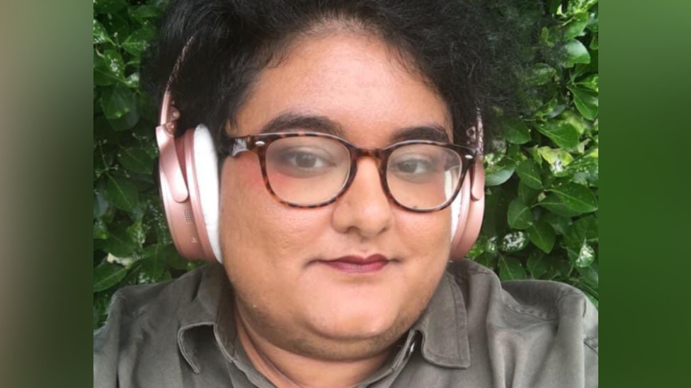 Noor Pervez takes a selfie, wearing glasses and headphones. They have dark brown hair.