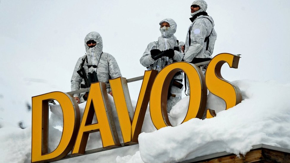Armed security personnel stand guard on the rooftop of a hotel, next to letters reading "Davos"