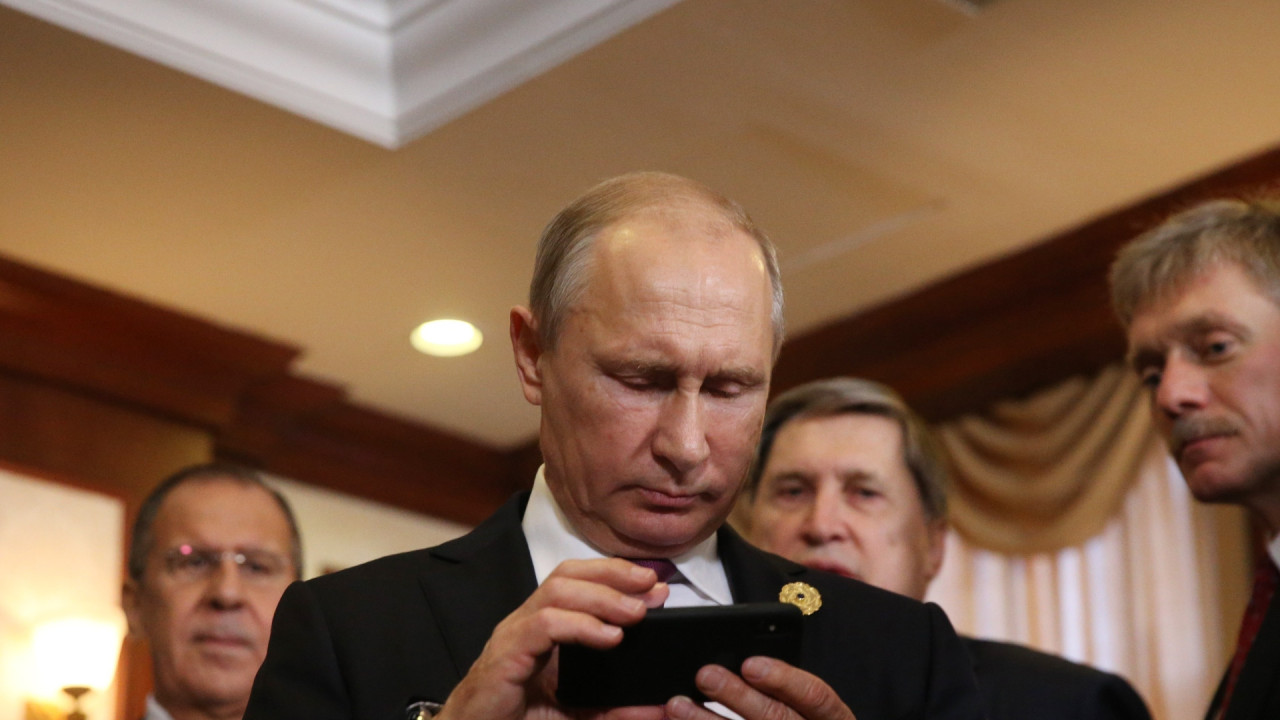 Vladimir Putin examines an iPhone in the company of spokesman Dmitri Peskov (right) and Foreign Minister Sergei Lavrov (left)