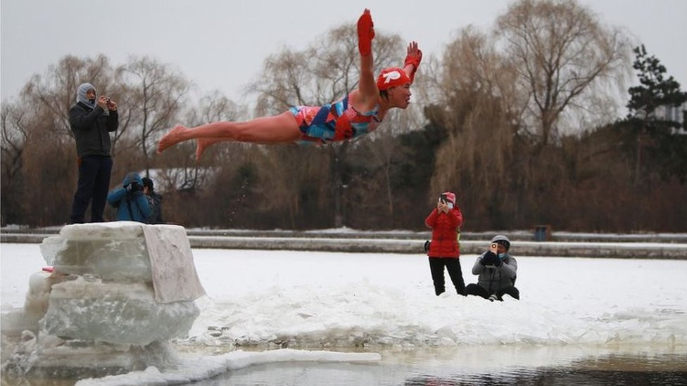 A swimmer suspended in the air mid-dive into a frozen lake