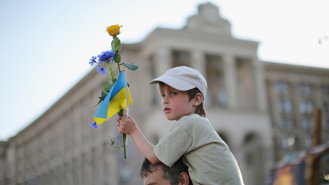 Ukrainian boy on father's shoulders holding a Ukrainian flag and a flower