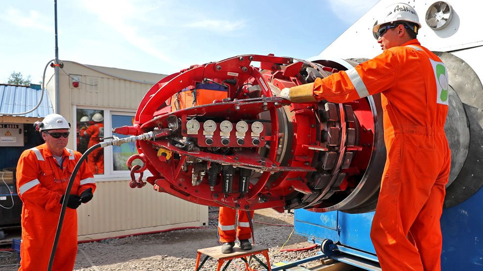 Two men in boiler suits working with a large piece of equipment, with pressure valves visible