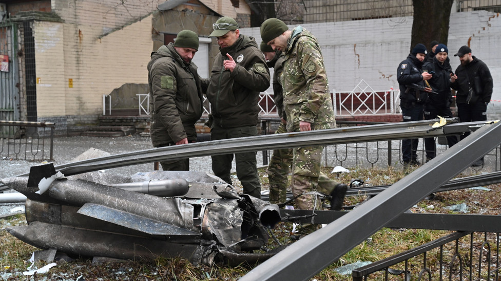 Police and security personnel inspect the remains of a shell in a street in Kyiv on 24 February 2022