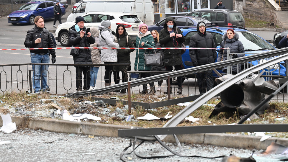 People react standing behind the cordoned off area around the remains of a shell in Kyiv on 24 February 2022