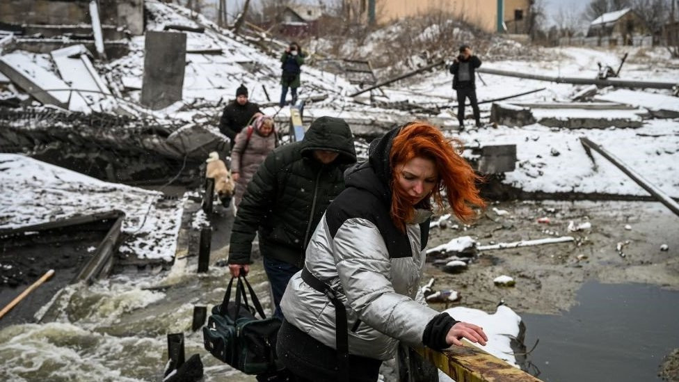 Civilians cross a river on a blown up bridge on Kyiv's northern front on March 1, 2022
