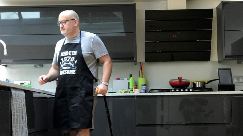 Ian Taverner standing in his kitchen with his walking stick