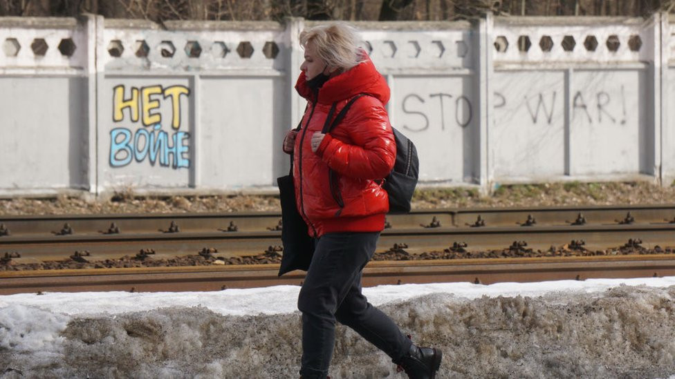 A woman walking past a sign saying "Stop war!" in Moscow