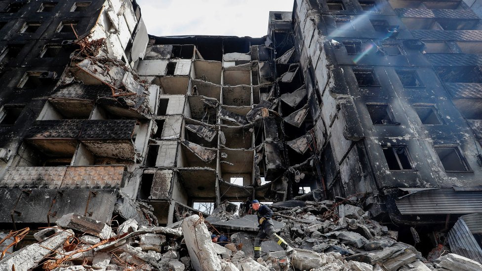 An emergency worker strides across rubble in front a a destroyed building