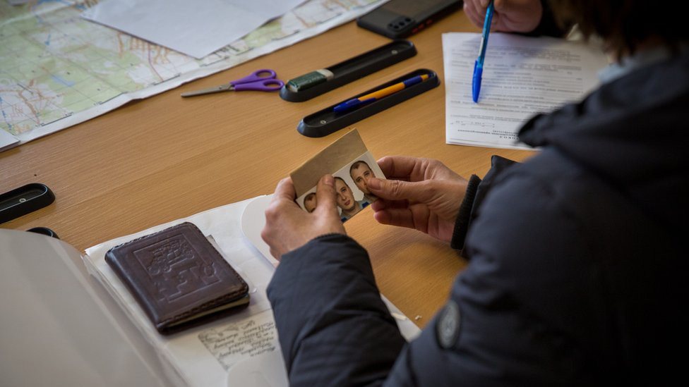 Olena Kuksa holds passport photographs of her missing husband at the police station.