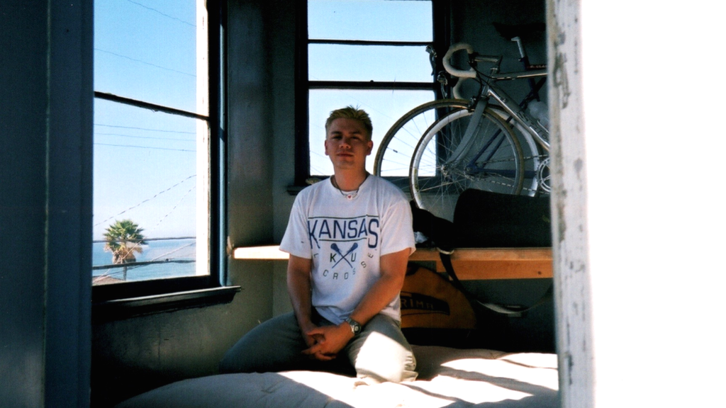 Tom Justice sitting in front of windows overlooking a beech with two bicycles hanging on the wall