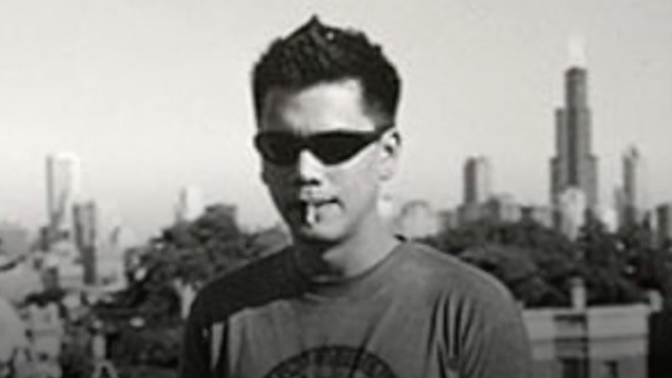 Tom Justice standing in front of the Chicago skyline with a cigarette in his mouth