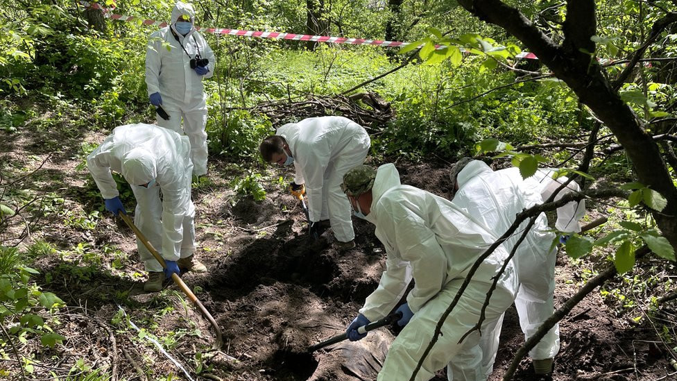 A Ukrainian forensic team remove a Russian soldier from a shallow grave on the outskirts of Kyiv
