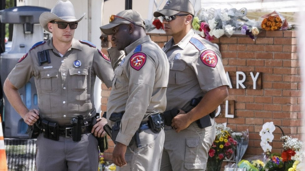 Officers stand near a memorial of flowers at the scene of the mass shooting at the Robb Elementary School in Uvalde, Texas on 25 May