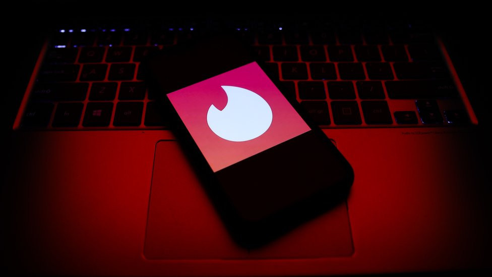 A mobile phone showing the Tinder logo sits on a laptop keyboard.