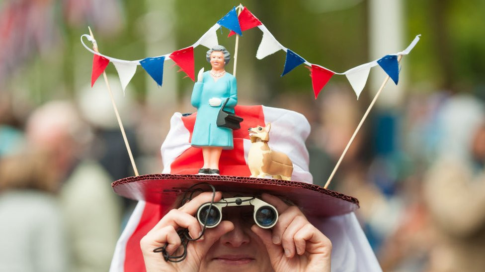 A woman in a fancy dress hat featuring Queen Elizabeth II and a corgi, pictured during the Diamond Jubilee concert at Buckingham Palace in 2012