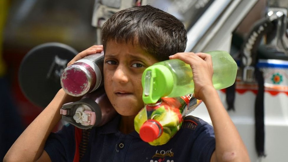 A boy carries water bottles on his return from school during a hot summer day in Rawalpindi, Pakistan