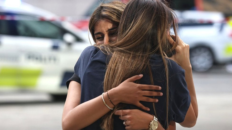 Two distressed women hug outside a Copenhagen shopping centre