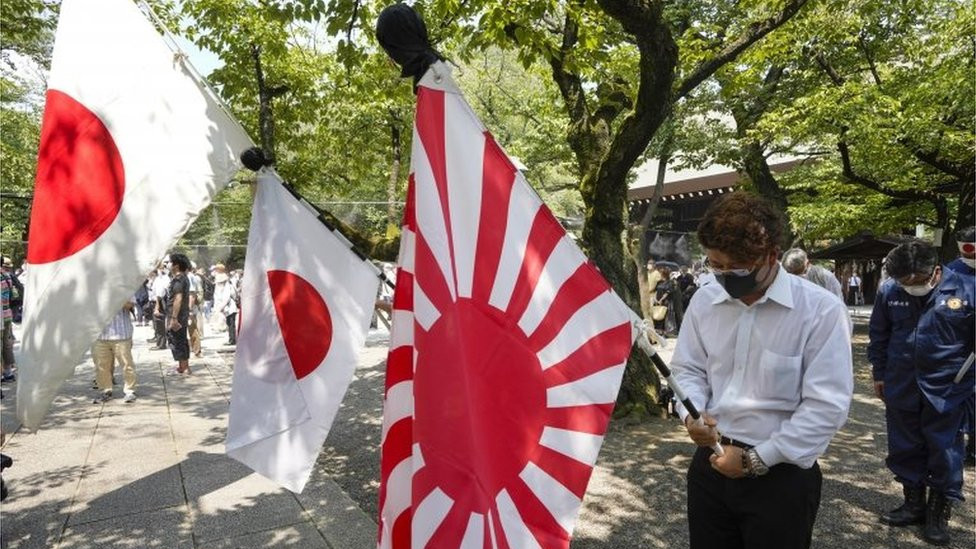 People holding Japan"s national flags and the rising sun flag offer one minute silence for the war dead at Yasukuni Shrine