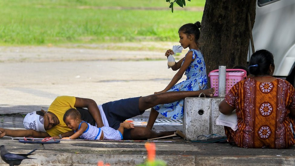 A Sri Lankan girl drinks tea from a plastic bag as a man attends to a crying baby while a woman looks on besides a pavement next to a road at Colombo, Sri Lanka. 21 May 2022.