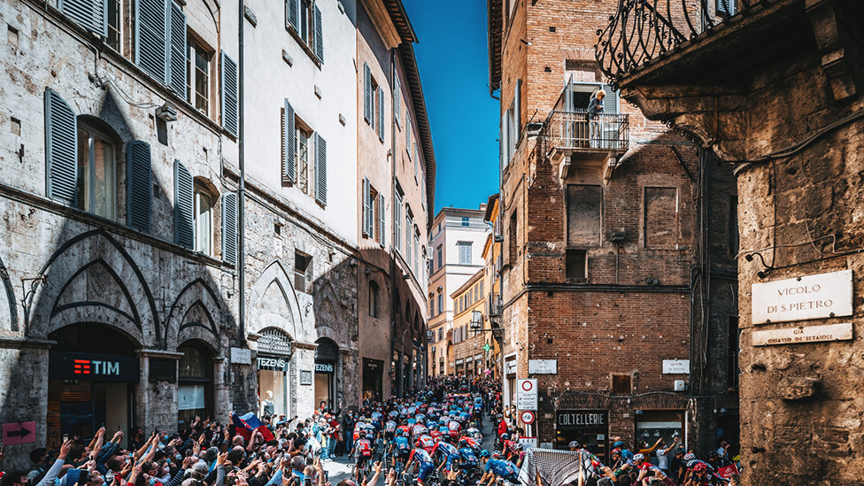 Gledaoci u uskoj ulici u italijanskoj Sijeni gledaju bicikliste dok voze 12. etapu takmičenja Điro d' Italija 2021. godine