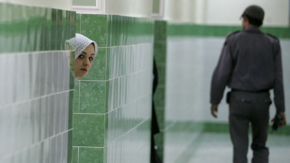 Iranian inmate peers from behind a wall as a guard walks by at the female section of the infamous Evin jail