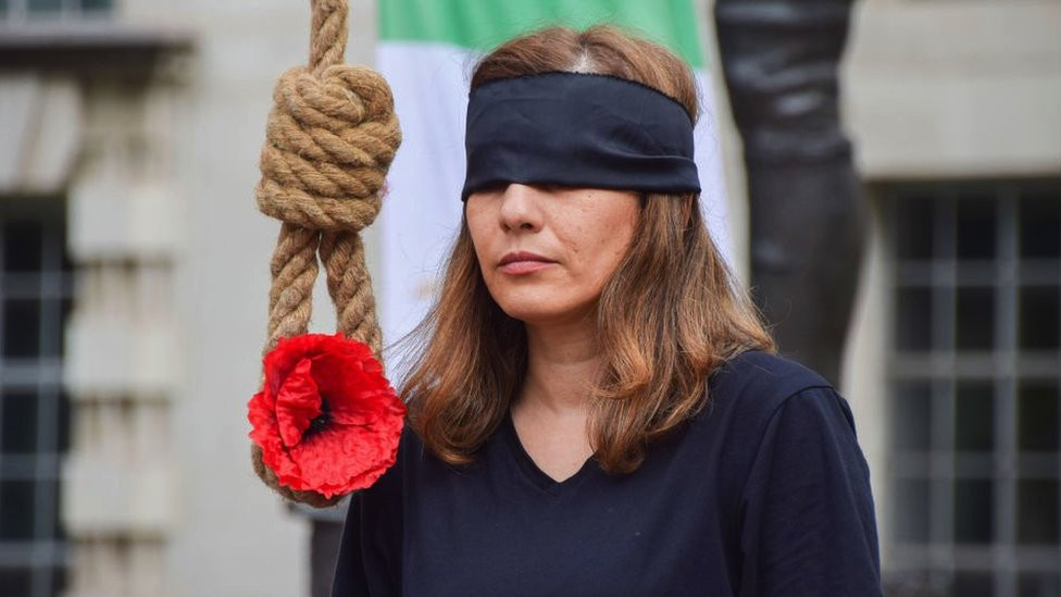 A woman stands next to a noose during a protest