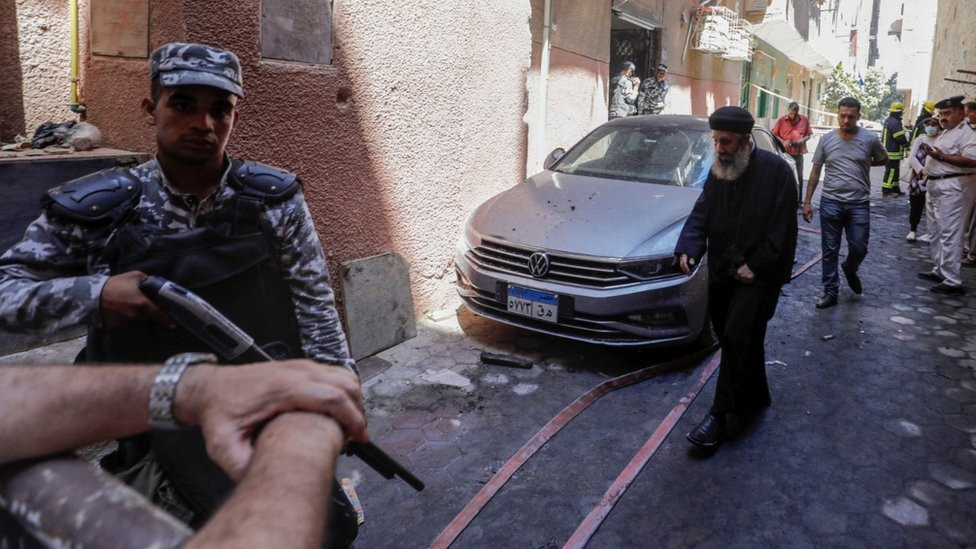 People and policemen gather near the scene where a deadly fire broke out at the Abu Sifin church