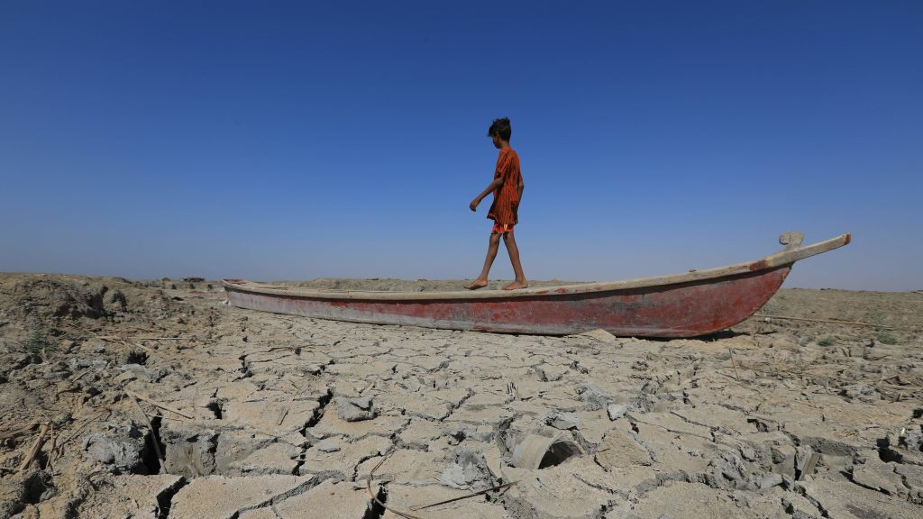 A boy walks on a boat left lying on the dried-up bed of a section of Iraq's receding southern marshes of Chibayish in Dhi Qar province, on June 28, 2022. - Iraq's drought reflects a decline in the level of waterways due to the lack of rain and lower flows from upstream neighboring countries Iran and Turkey.