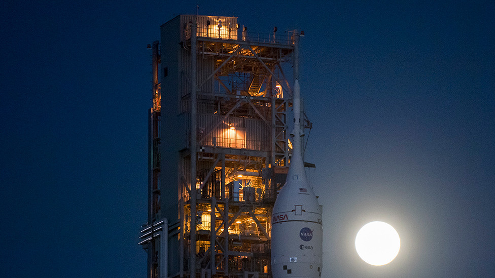 SLS-Orion at the launch pad with the Moon glowing in the sky and illuminating the area