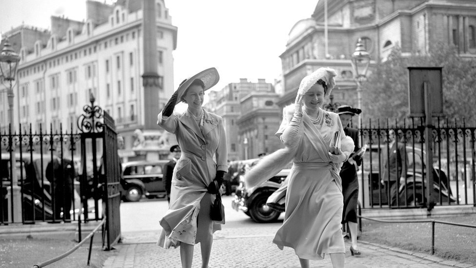 Queen Elizabeth and Princess Elizabeth hold on to their hats as they arrive at Westminster Abbey to attend the wedding of Lady Caroline Montagu-Douglas-Scott to Mr Ian Hedworth Gilmour