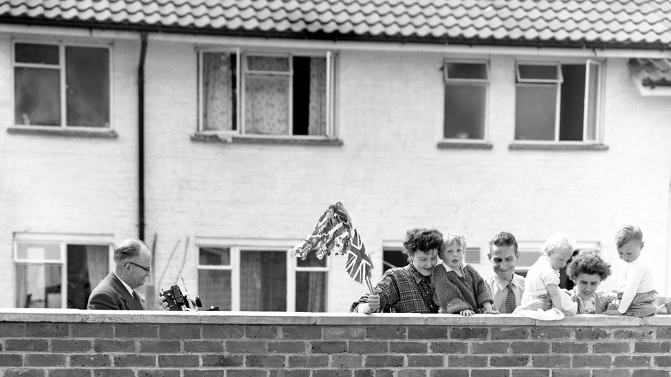A Union Jack planted in the garden caught the Queen's attention, but she is the object of the neighbours' gaze. They watched as she arrived to visit the home of Mr and Mrs Eddie Hammond at Crawley New Town, Sussex after opening Gatwick Airport. 1958