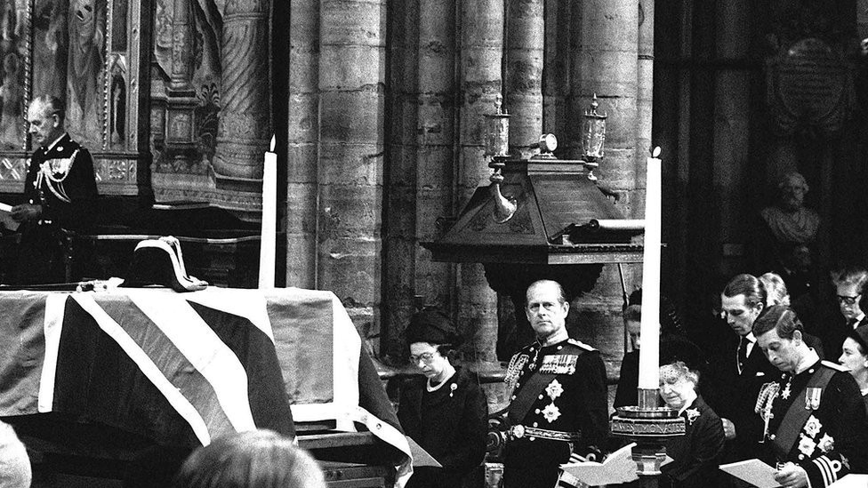 The flag-draped coffin of Lord Mountbatten rests on a catafalque during the funeral service in Westminster Abbey. Royal mourners (l-r) Queen Elizabeth II, her husband the Duke of Edinburgh, Queen Elizabeth, The Queen Mother, and the Prince of Wales, 5 September 1979