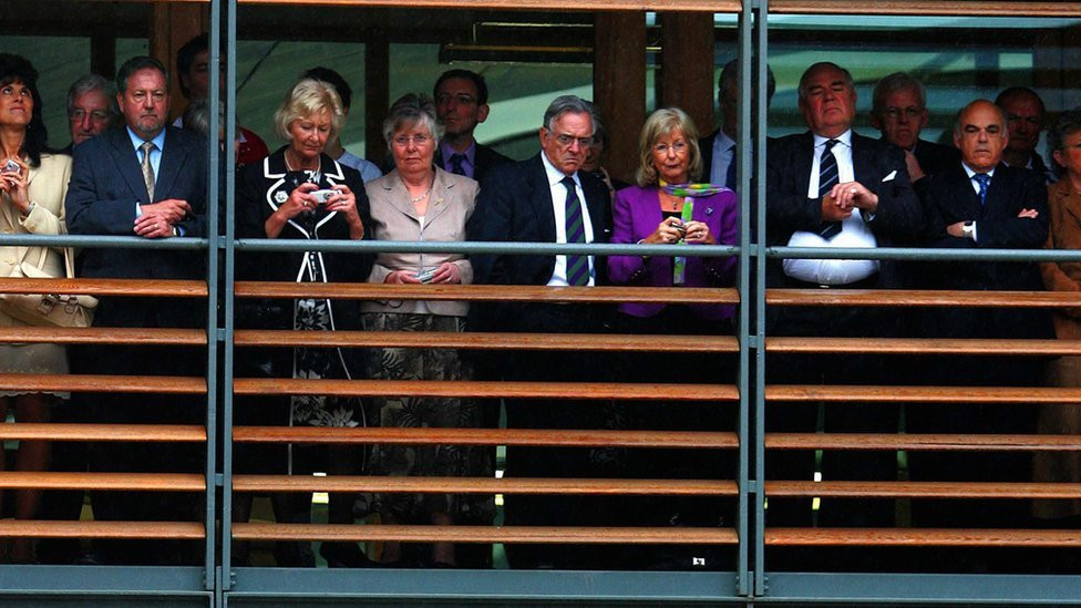 Queen Elizabeth II stands in the rain as guests take shelter at the opening of the Lawn Tennis Associations new headquarters in Roehampton, London, 2007