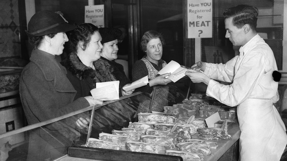 A shop assistant in a butcher's shop in south London cuts a coupon out of a customer's ration book on the first day of rationing in Britain