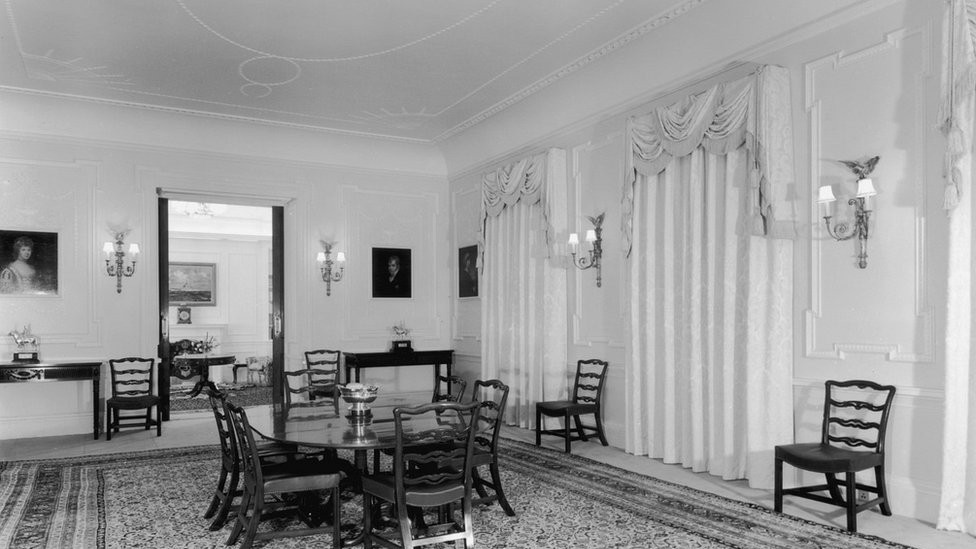 The dining room of Clarence House in London, 1949. The house was built in 1825-27 by John Nash for the Duke of Clarence, later King William IV. The dining table and chairs are mahogany and the curtains are white figured damask