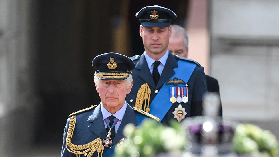 King Charles III and Prince William, Prince of Wales walk behind the coffin of Queen Elizabeth II during a procession from Buckingham Palace to the Palace of Westminster