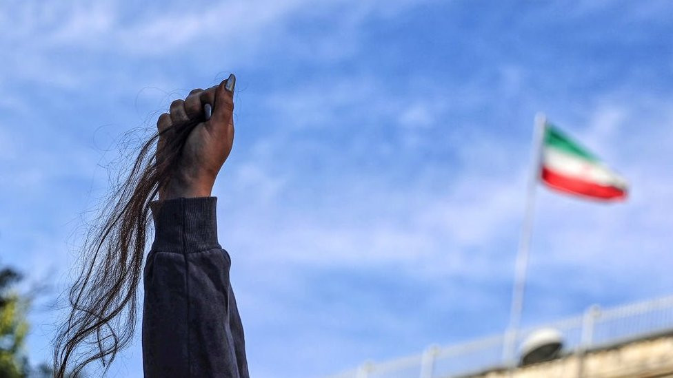 Woman holds hair in the air with Iranian flag in the background