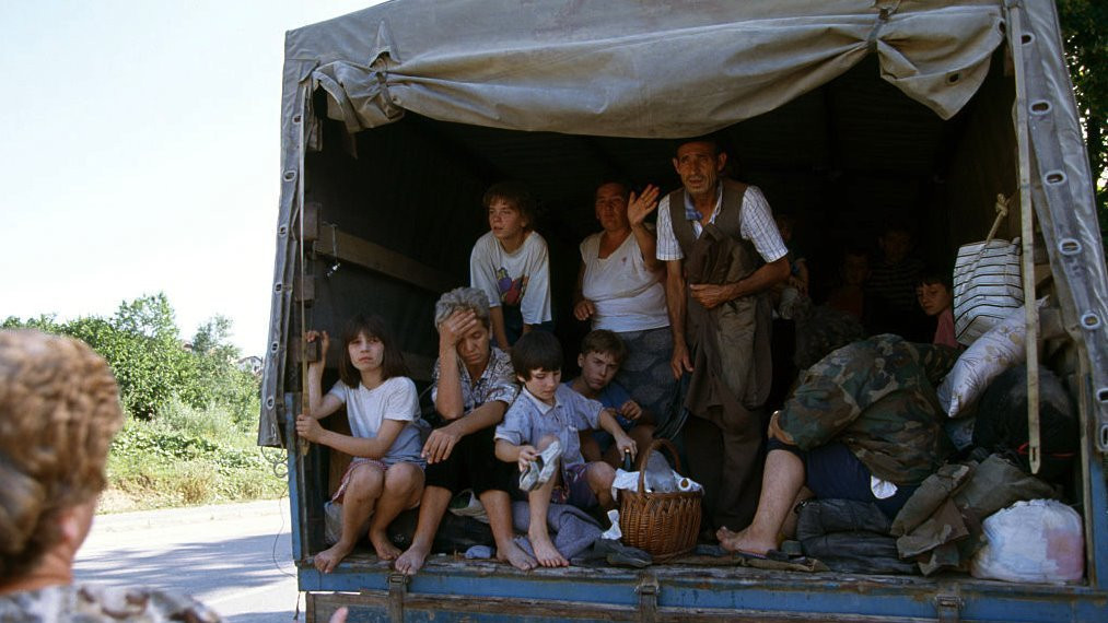 An extended Bosnian refugee family waves good-bye to a relative as they flee the riots in Mostar in a cargo vehicle, July 29, 1992