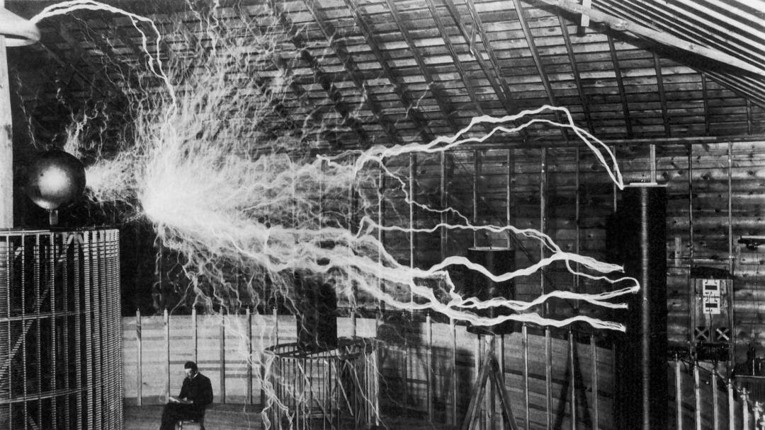 Inventor and scientist Nikola Tesla in his lab while his magnifying transmitter high voltage generator produces bolts of electricity. December 1899