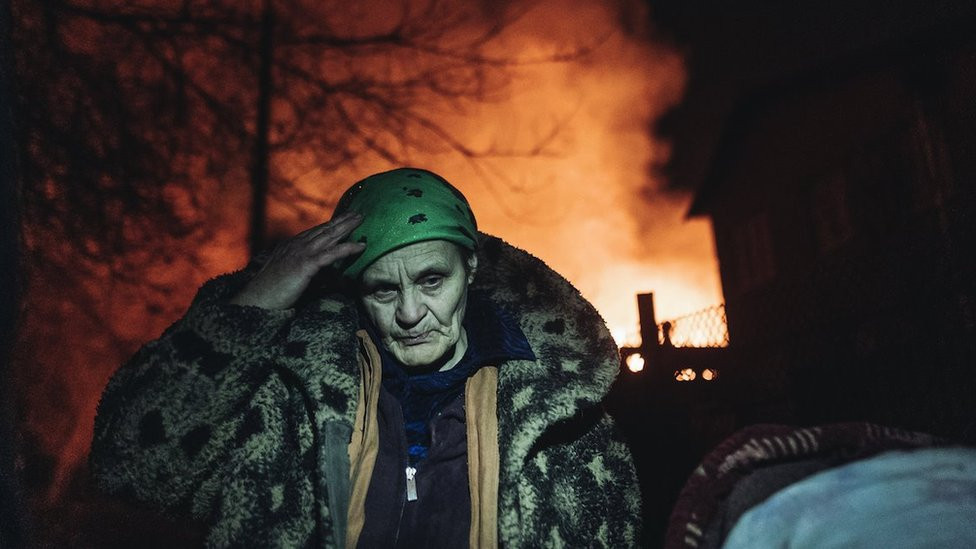 A citizen is seen in front of burning houses as emergency service workers extinguish a fire after shelling on the Bakhmut frontline in Ivanivske