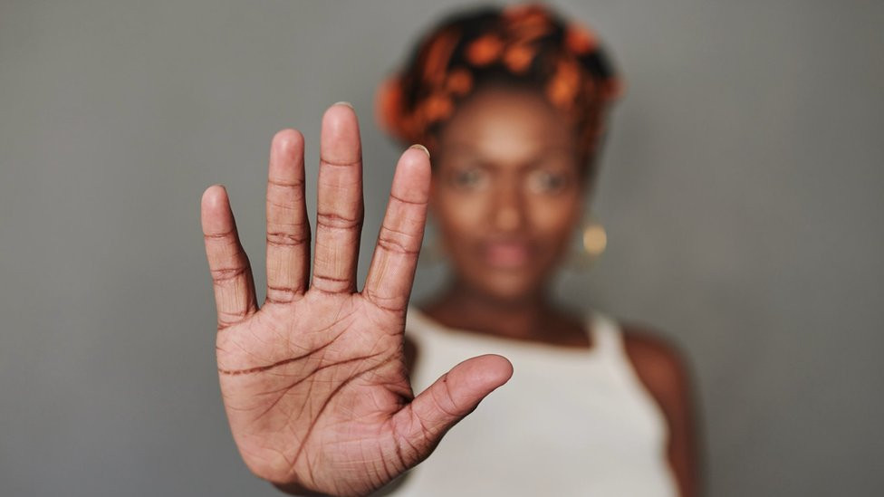 A woman makes a stop sign towards the camera