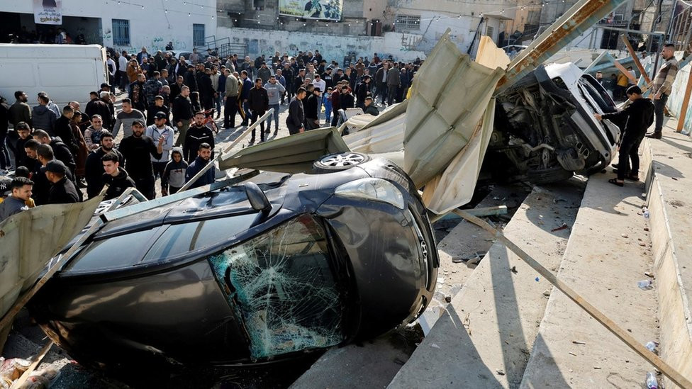 Palestinians inspect damaged vehicles and buildings in Jenin, in the occupied West Bank, after nine Palestinians were killed in an Israeli military raid (26 January 2023)