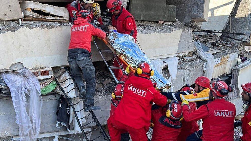 Rescuers carry a woman after she was evacuated from under a collapsed building following an earthquake in Kahramanmaras, Turkey