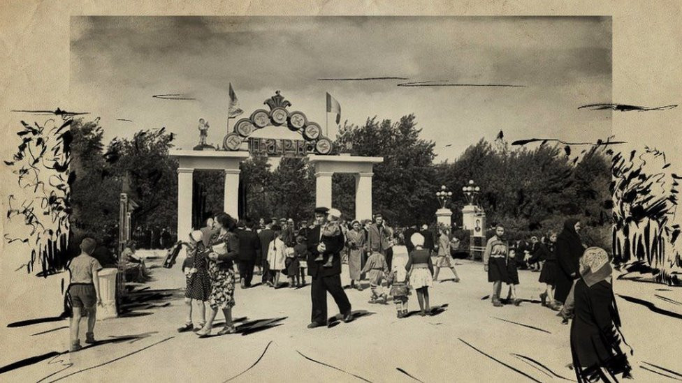 People mill about a park gate