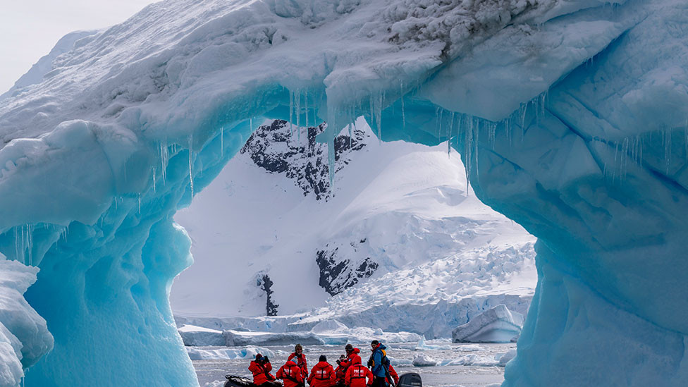 Tourists exploring an iceberg arch in Cierva Cove along the west coast of Graham Land, Antarctic Peninsula, Antarctica