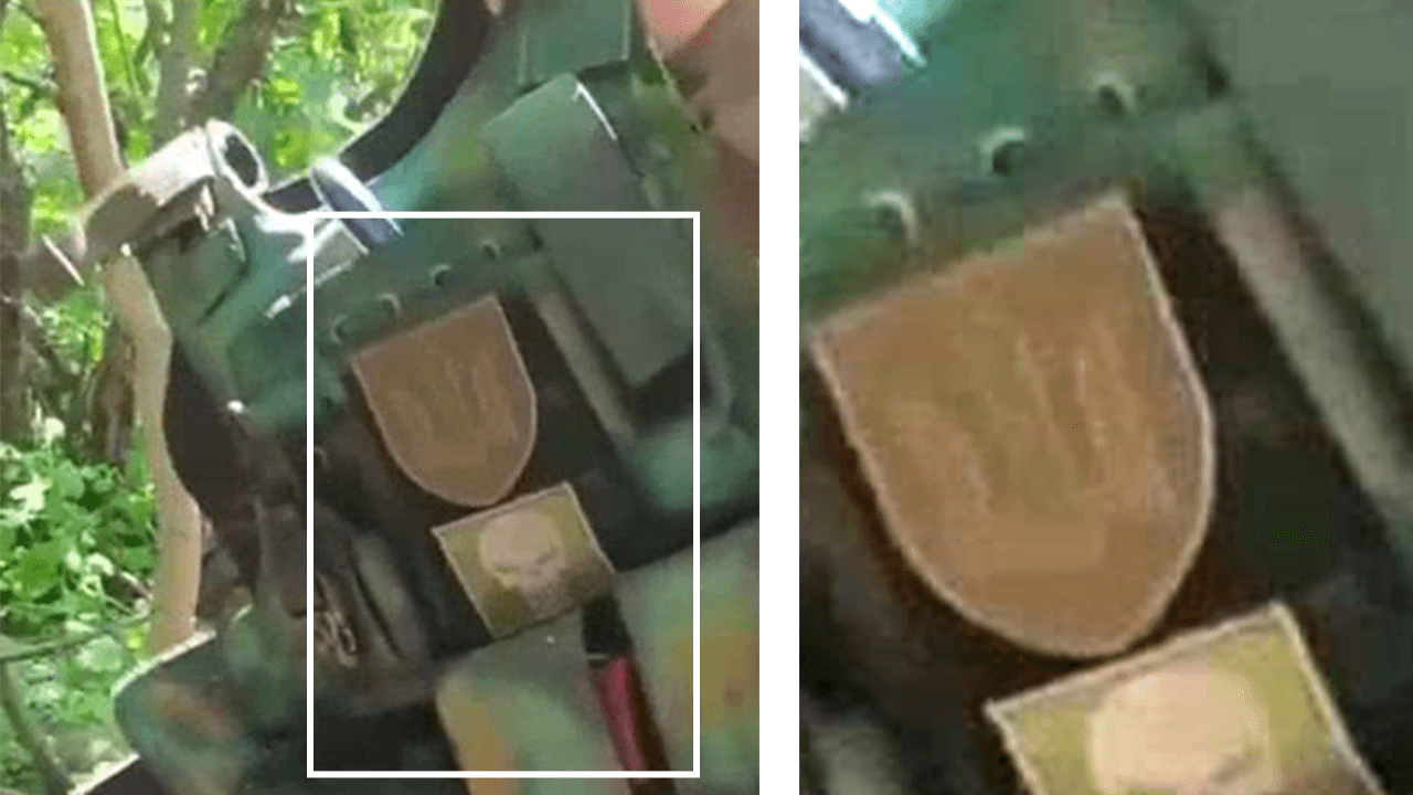 Video frame showing patches worn on a piece of body armour held up in front of the camera