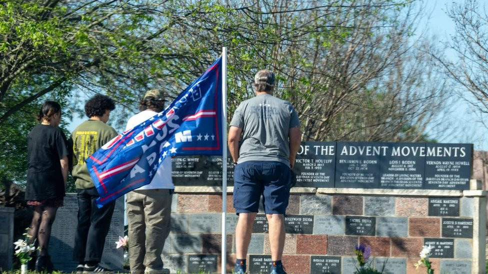 People stand with heads bowed before a monument to the dead at Waco